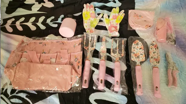 A YANZI gardening tool set laid out on a bed, including pink tools, floral gloves, and a matching apron