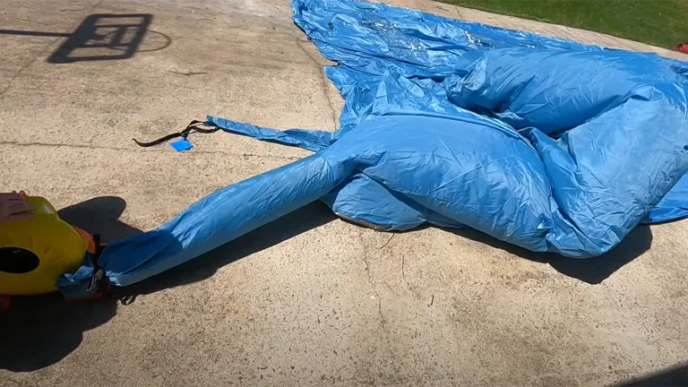 A deflated blue inflatable paint booth lies on concrete, with a blower attached, ready for inflation.