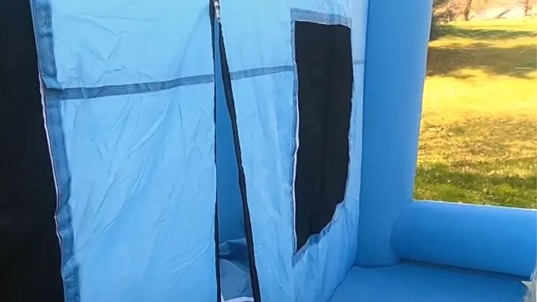 Close-up of the doorway of a blue inflatable paint booth with black mesh windows and reinforced seams.