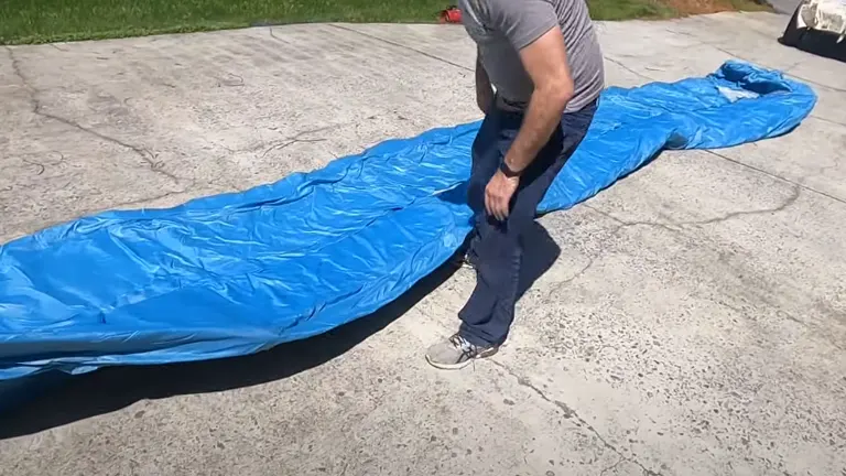 A person is unfolding a blue inflatable structure on a concrete surface in preparation for setting it up.