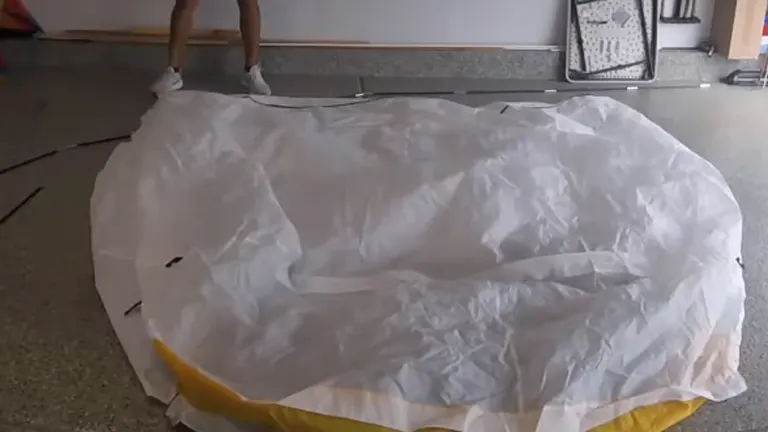 A Wagner Spraytech spray shelter in the process of being set up or taken down on a garage floor, with its white and yellow cover partially collapsed.