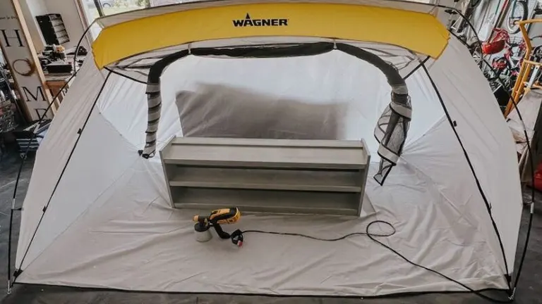 A Wagner Spraytech spray shelter set up in a workshop, with a grey furniture piece inside and a spray gun resting on the shelter's integrated floor.