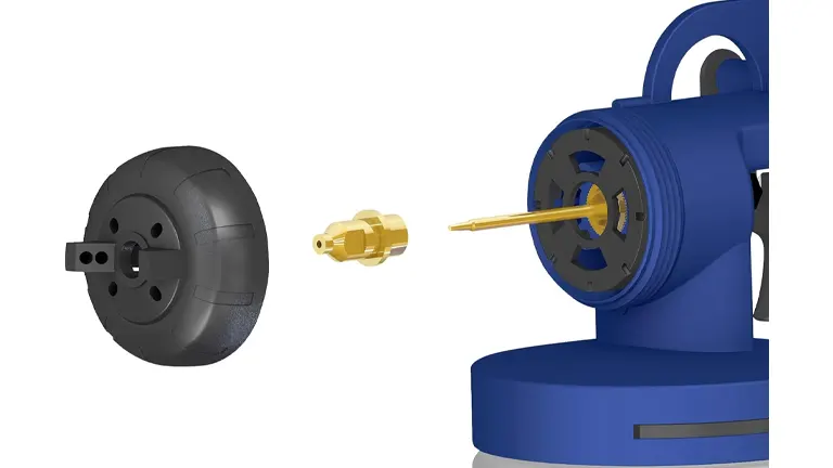 A close-up view of a black spray gun tip and a detached brass nozzle, with the blue body of a paint sprayer in the background.