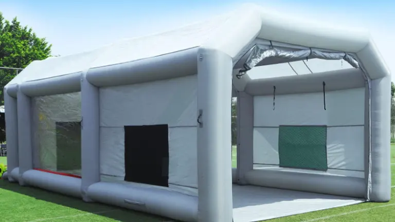 A spacious, inflatable, grey paint booth with a clear viewing window and a black entrance flap, set up outdoors.