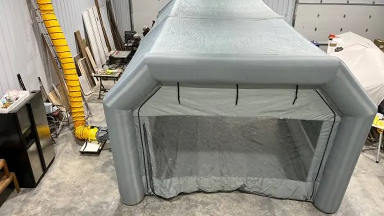 Inflatable grey paint booth with transparent front and hooks for lighting installed in an indoor workspace.