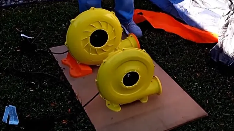 Two yellow inflation blowers on the ground, possibly for an inflatable structure, with a person’s feet visible in the background.