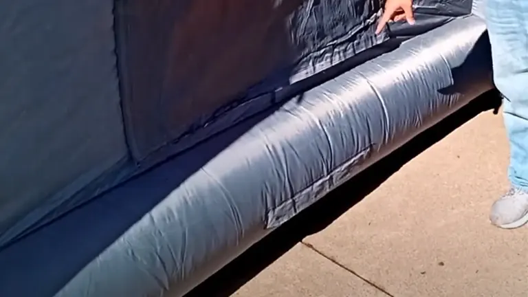 A person’s hand pressing down on the edge of an inflated structure, possibly part of an inflatable paint booth, showcasing its material and thickness.