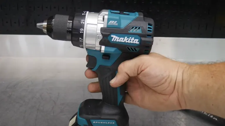 A person's hand is shown holding a Makita BL brushless cordless drill, highlighting its compact size and ergonomic grip against a workbench backdrop.