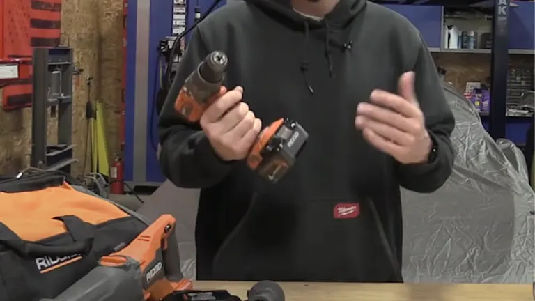 A person in a workshop holding an orange RIDGID cordless hammer drill with a soft carrying case in the foreground.