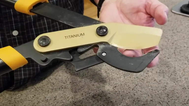 A hand holding a Fiskars PowerGear Bypass Lopper with a titanium blade and gear mechanism, the yellow and black handles indicative of its premium build and design.