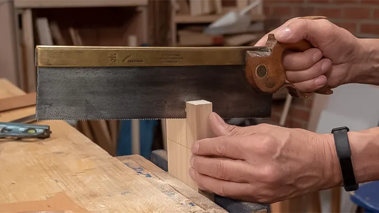 Hands using a backsaw to make a precise cut on a wooden piece clamped to a workbench, a basic woodworking skill