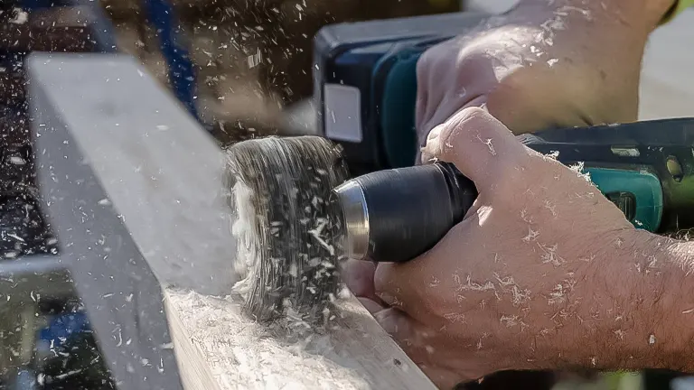 Close-up of a woodworker using an electric sander on a plank, with sawdust flying, showcasing an essential woodworking finishing technique