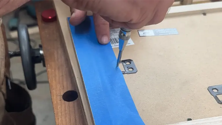 Hand marking a measurement on blue painter's tape applied to a wooden board, showcasing precision in woodworking