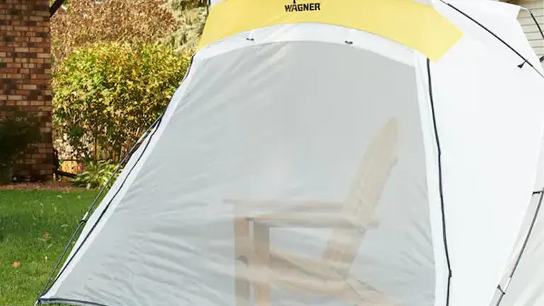 A Wagner Spraytech spray shelter outdoors, with a chair inside visible through the semi-transparent front, ready for painting.