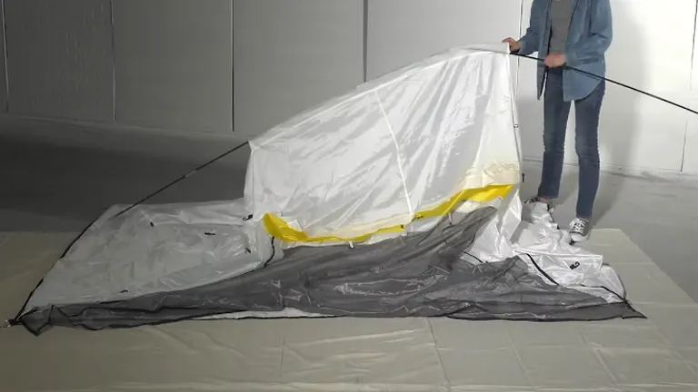 A person in casual attire is setting up a Wagner Spraytech spray shelter, with the structure partially unfolded on the floor.