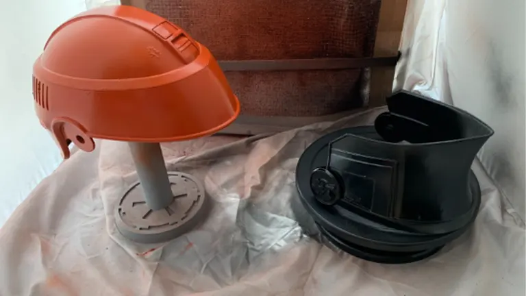 Two painted objects, one orange and one black, drying on a protective sheet, with the orange item resembling a lamp and the black one shaped like a funnel.