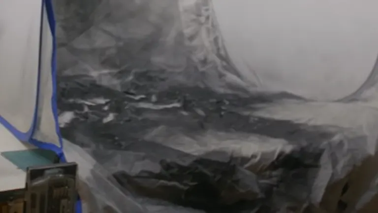 A blurred image showing a plastic-covered area, likely part of a makeshift spray painting setup, with visible creases and folds in the plastic sheeting.