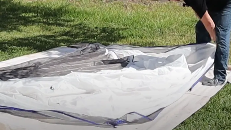 Person setting up a collapsible HomeRight Spray Shelter on grass, partially assembled with visible framework.