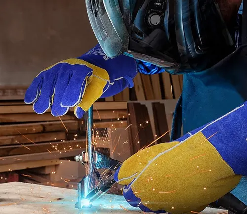 Welder using RAPICCA blue and tan heat-resistant welding gloves during a welding process with sparks flying.