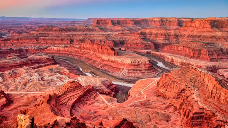 Sunset casting warm hues over the intricate layers and winding river of a vast red rock canyon.