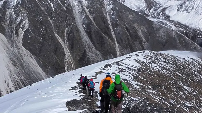 A group of hikers with colorful backpacks trekking along a snowy mountain ridge in Bhutan, surrounded by a stunning panorama of rugged, snow-covered peaks.