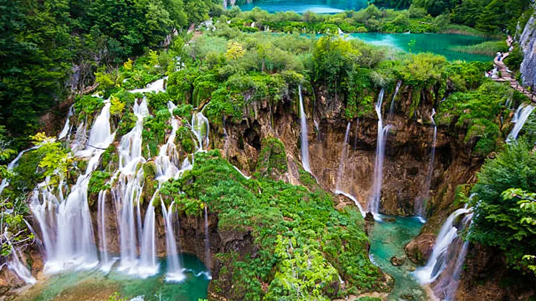 Serene view of Plitvice Lakes National Park with multiple waterfalls cascading into turquoise pools, surrounded by lush, green forested landscape.