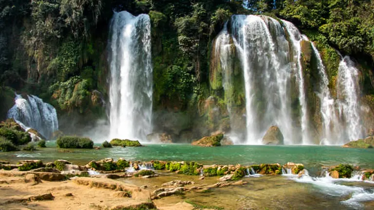 Spectacular view of Ban Gioc–Detian Falls with powerful twin waterfalls cascading into a serene emerald pool surrounded by verdant forested cliffs.