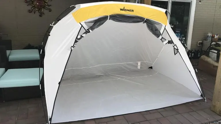 A white and yellow Wagner Spraytech spray shelter with a curved design, set up on a patio, ready for painting projects.