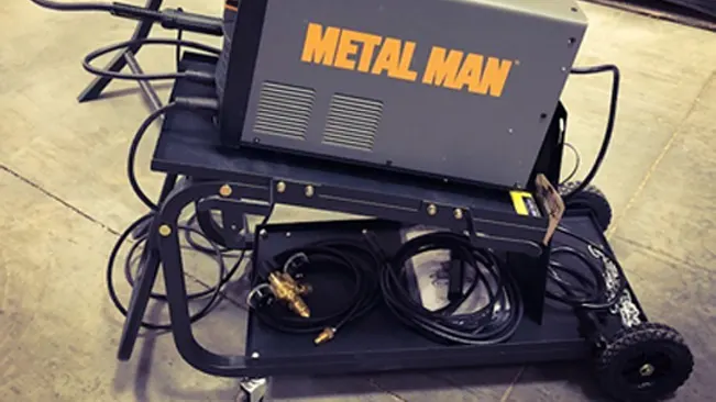 Metal Man welding equipment and cables on a UWC2XL Universal Welding Cart with a fold-down handle in a workshop setting.