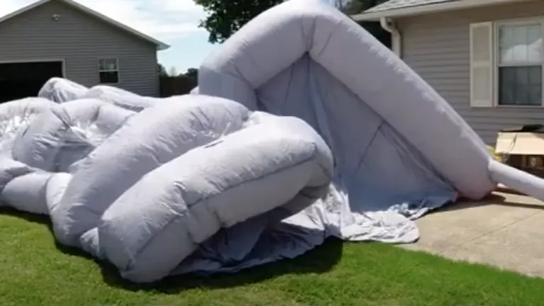 A large inflatable structure is partially deflated on a lawn, with its framework collapsing onto the grass.