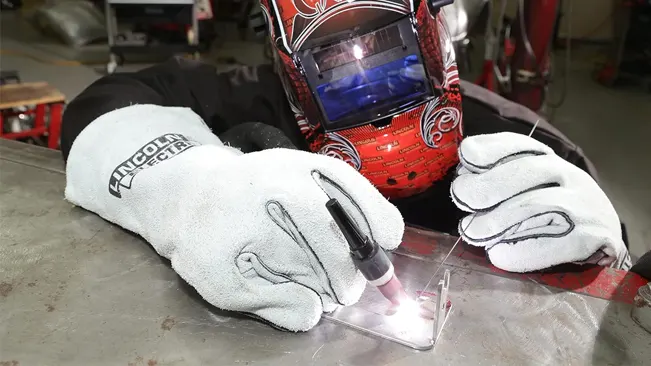Welder wearing Lincoln Electric KH641 gloves and a protective helmet while welding a metal sheet.