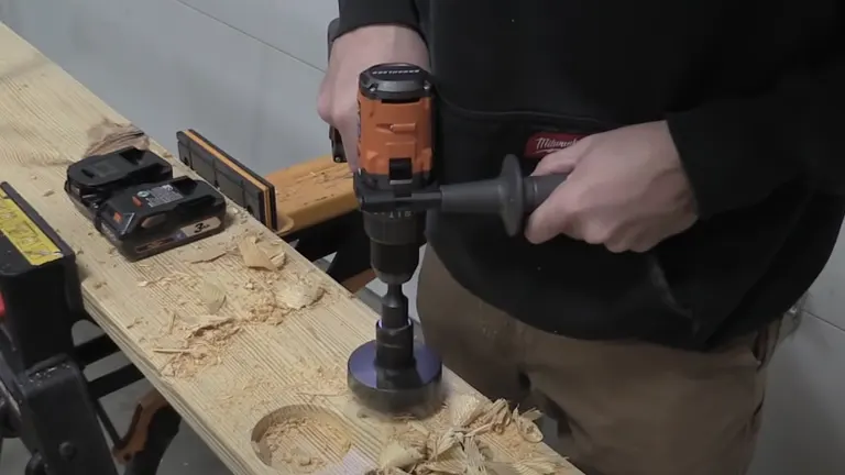 A person using a RIDGID cordless hammer drill on a wooden surface, with wood shavings around and a battery pack nearby.