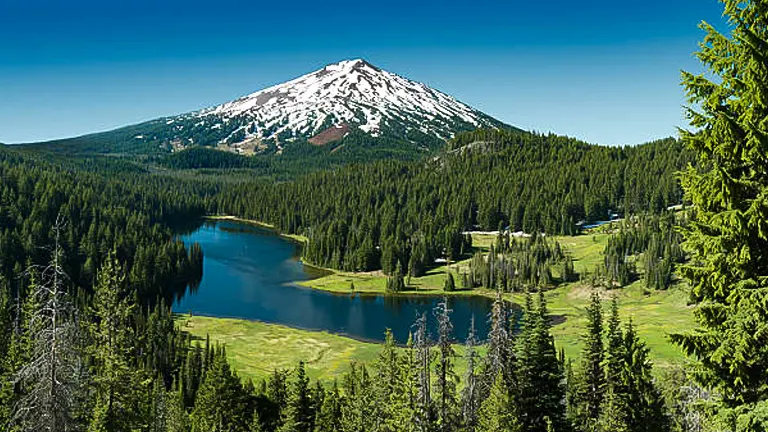 Mount Bachelor looms over a peaceful alpine lake in Deschutes National Forest, with lush evergreen forests in the foreground.