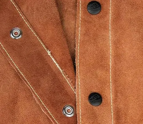 Detail of a brown leather welding jacket showing silver snap buttons and contrasting stitching.