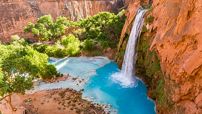Havasu Falls cascading into a stunning turquoise blue pool surrounded by lush greenery and red canyon walls, creating an oasis in the arid landscape.