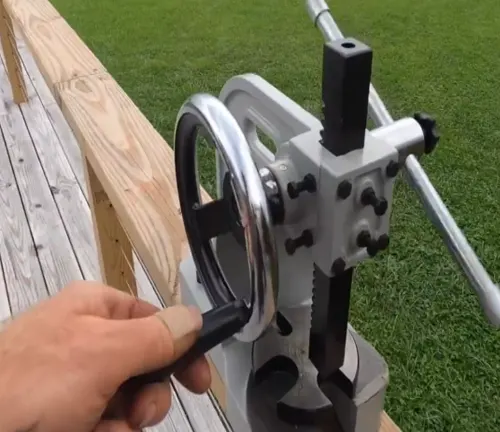 A hand turning the wheel of a silver metal arbor press on a wooden bench