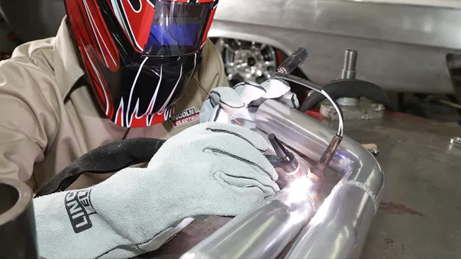Welder in a mask using Lincoln Electric KH641 gloves while welding a metal pipe.