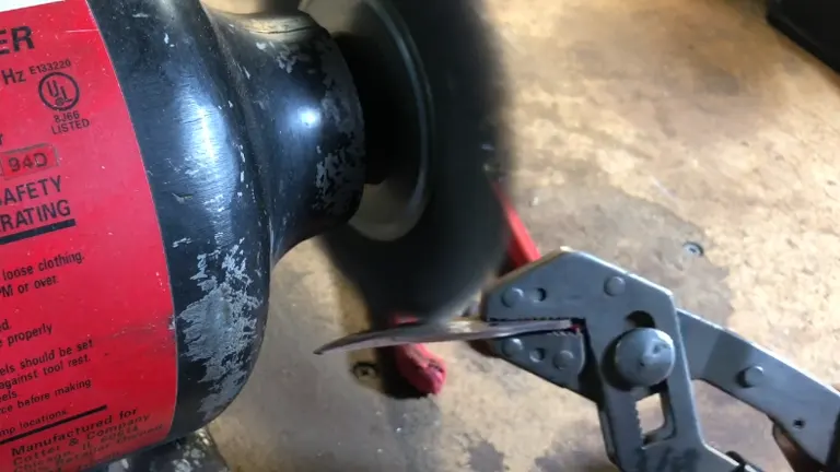A close-up of a pruning shear being sharpened on a bench grinder, with focus on the blade against the rotating grinding wheel.