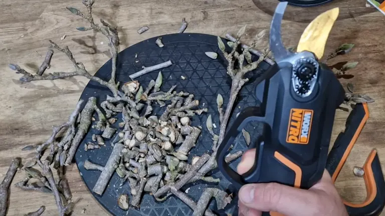 A Worx NITRO pruning shear is shown next to a pile of freshly cut branches and twigs on a wooden surface, highlighting the tool's cutting results.