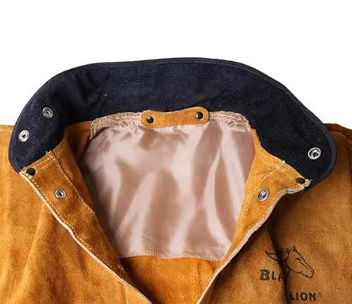 Close-up of the inside collar of a welding jacket with a denim exterior, tan leather trim, and silver grommets.