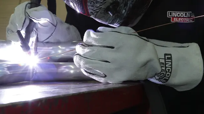Close-up of a welder's hands wearing Lincoln Electric KH641 gloves, welding with a bright arc light.