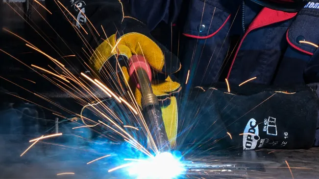 Welder using a TOPDC 16-inch welding glove amidst sparks and bright welding light.