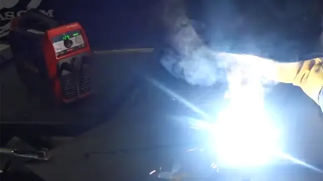Intense welding light from a torch with smoke, next to a Fronius AccuPocket 150 Welder displaying '125' on the screen.

