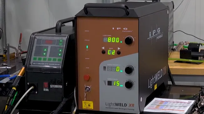 IPG LightWELD XR Handheld Laser Welder on a workbench, displaying settings on its screen, with other equipment in the background.