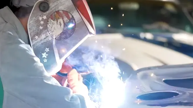 Welder using a Jackson Safety auto-darkening helmet with a patriotic design while welding, with visible blue welding light.