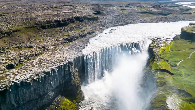 Aerial view of Dettifoss, a massive waterfall in Iceland, with voluminous water thundering down into the canyon below amidst a rugged landscape stretching into the distance.
