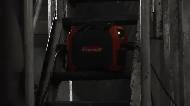 Fronius AccuPocket 150 TIG/Stick Welder positioned on a dark industrial staircase, with a red and black casing and a green power light.