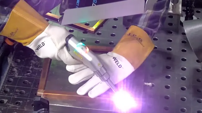 Hands in protective gloves using a LightWELD XR handheld laser to weld on a perforated work table with a bright light emission.