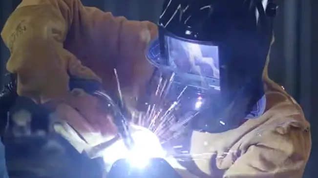 Welder in protective clothing using a welding torch, with sparks flying and a Weldcote Metals Ultraview helmet visible.