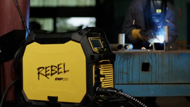 Esab Rebel EMP 205IC AC/DC Multi-Process Welder in a workshop setting with a person welding in the background.